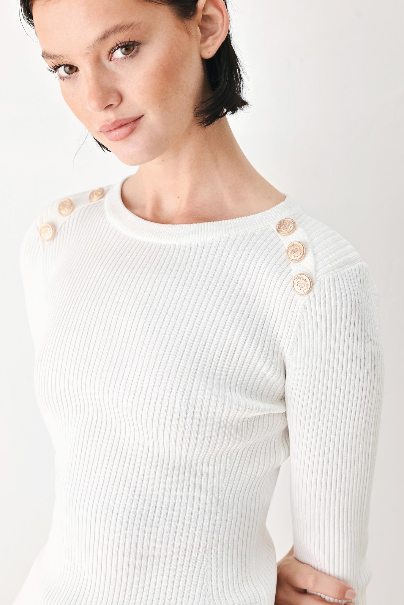 A woman modeling a white ribbed long-sleeve sweater with decorative gold buttons on the shoulders | FREEMARKET