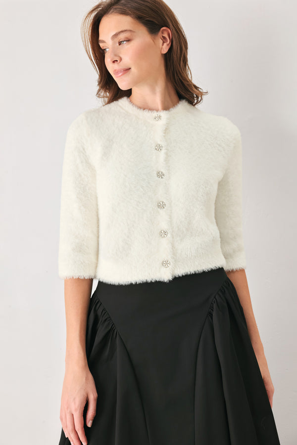 A woman wearing an off white fuzzy cropped cardigan with decorative silver buttons down the front | FREEMARKET