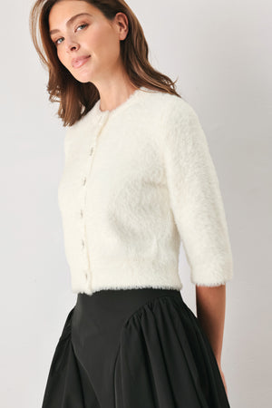 A woman wearing an off white fuzzy cropped cardigan with decorative silver buttons down the front | FREEMARKET