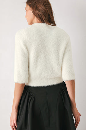 A woman wearing an off white fuzzy cropped cardigan with decorative silver buttons down the front | FREEMARKET