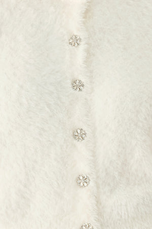A woman wearing an off white fuzzy cropped cardigan with decorative silver buttons down the front | FREEMARKET