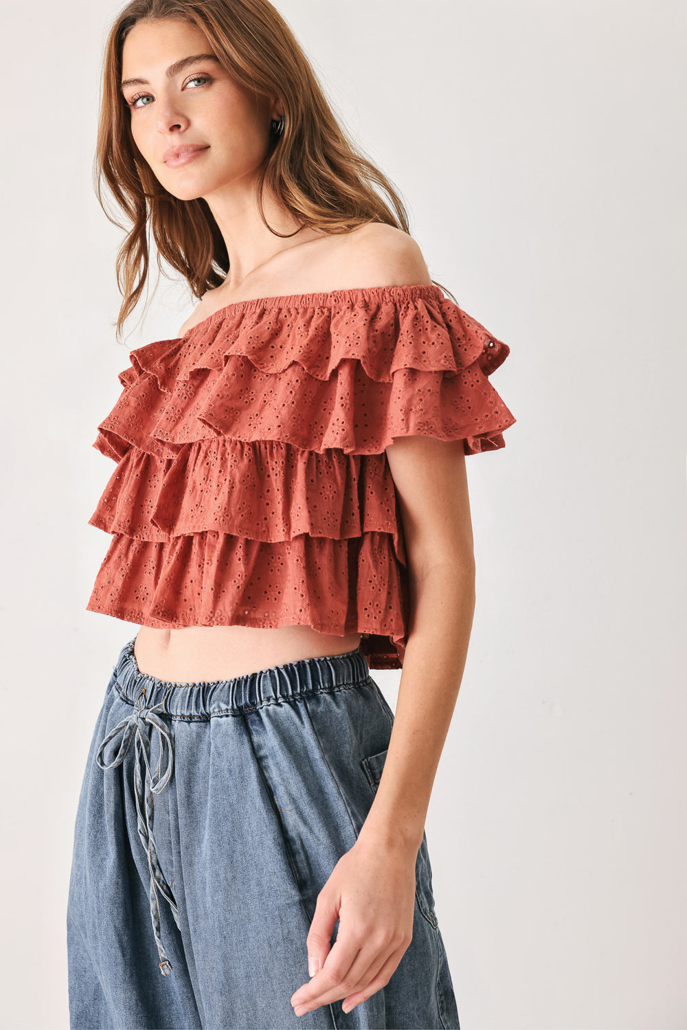 A woman wearing a terracotta-colored off-the-shoulder ruffled crop top | FREEMARKET