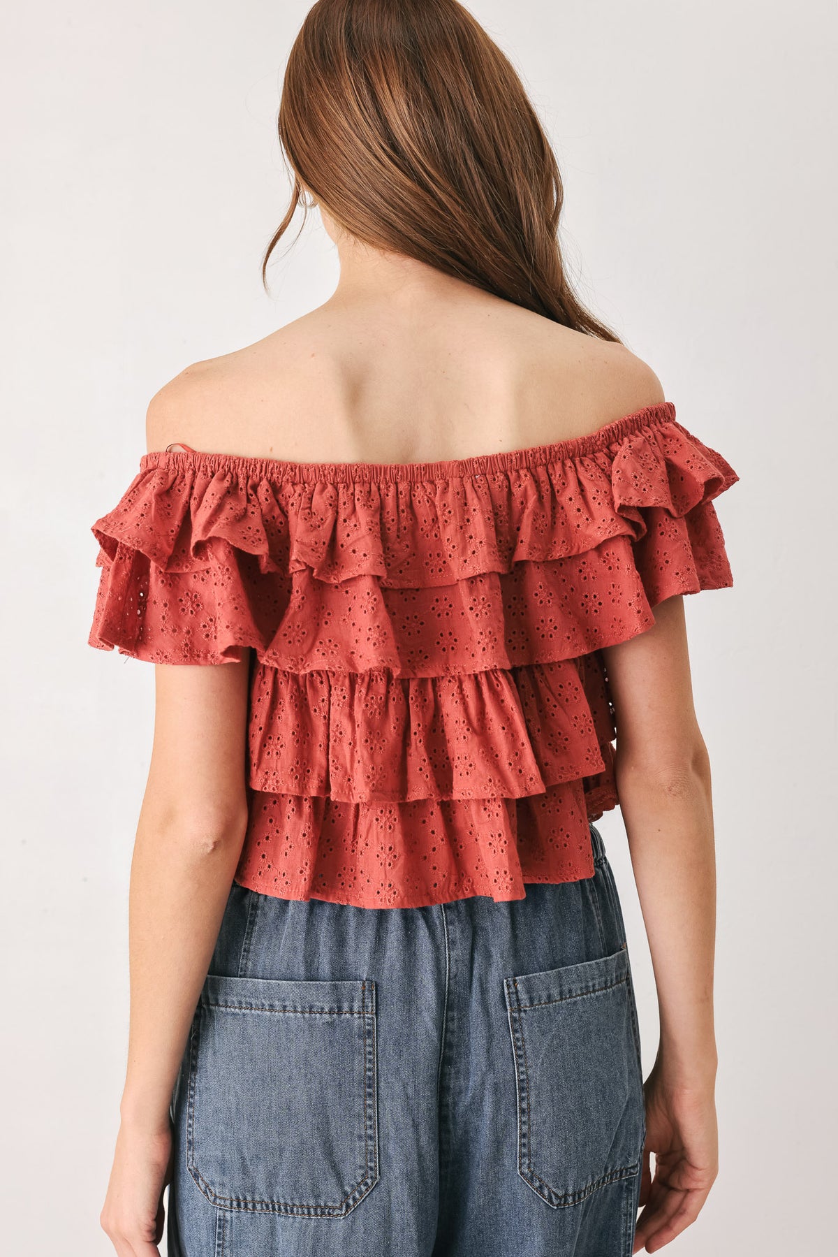 A woman wearing a terracotta-colored off-the-shoulder ruffled crop top | FREEMARKET