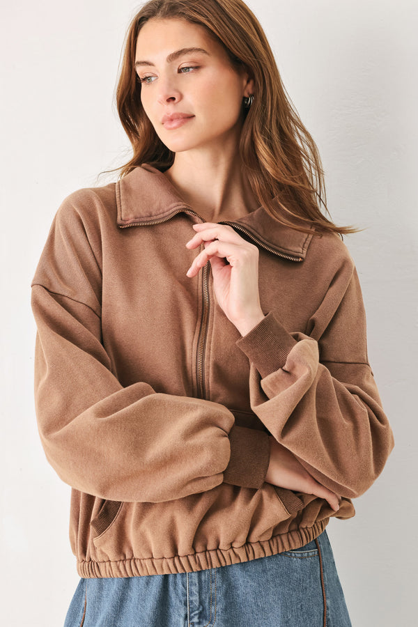 
A woman wearing a brown half-zip pullover sweatshirt with a collar and front pockets, paired with light blue jeans | FREEMARKET
