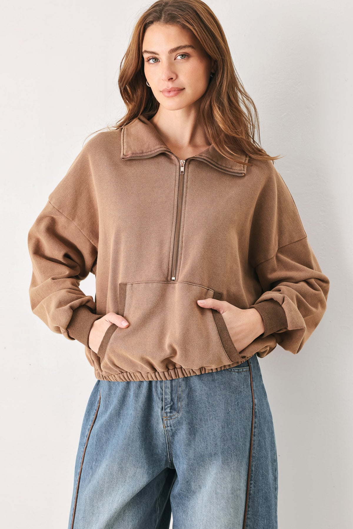 
A woman wearing a brown half-zip pullover sweatshirt with a collar and front pockets, paired with light blue jeans | FREEMARKET
