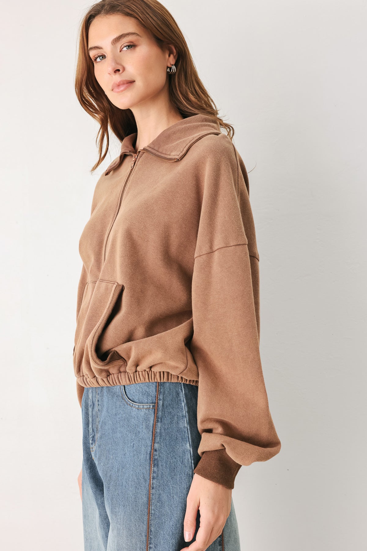 
A woman wearing a brown half-zip pullover sweatshirt with a collar and front pockets, paired with light blue jeans | FREEMARKET
