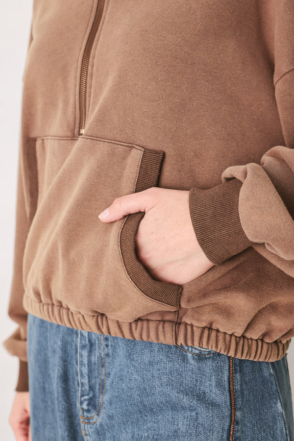 
A woman wearing a brown half-zip pullover sweatshirt with a collar and front pockets, paired with light blue jeans | FREEMARKET
