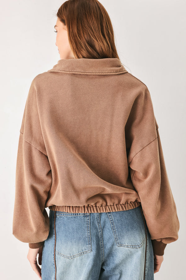 
A woman wearing a brown half-zip pullover sweatshirt with a collar and front pockets, paired with light blue jeans | FREEMARKET
