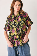 A woman wearing a black short-sleeve button-up shirt with a vibrant multicolor floral print in pink, yellow, and green | FREEMARKET