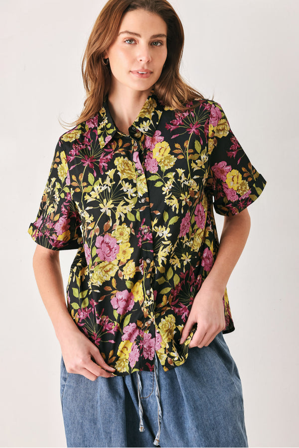 A woman wearing a black short-sleeve button-up shirt with a vibrant multicolor floral print in pink, yellow, and green | FREEMARKET