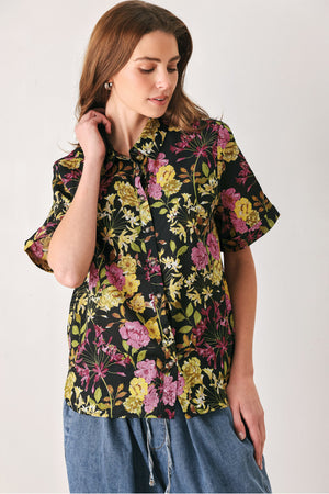 A woman wearing a black short-sleeve button-up shirt with a vibrant multicolor floral print in pink, yellow, and green | FREEMARKET