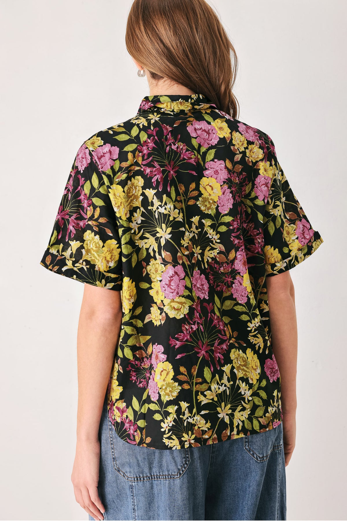 A woman wearing a black short-sleeve button-up shirt with a vibrant multicolor floral print in pink, yellow, and green | FREEMARKET
