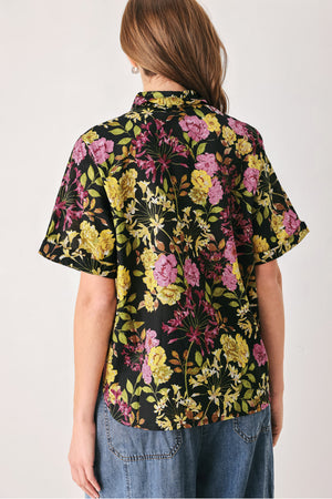 A woman wearing a black short-sleeve button-up shirt with a vibrant multicolor floral print in pink, yellow, and green | FREEMARKET
