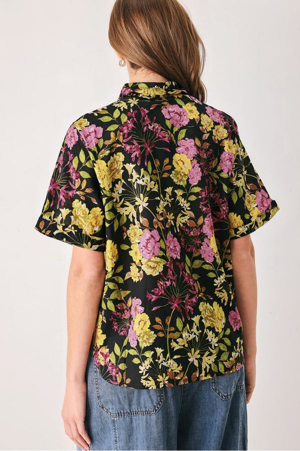 A woman wearing a black short-sleeve button-up shirt with a vibrant multicolor floral print in pink, yellow, and green | FREEMARKET