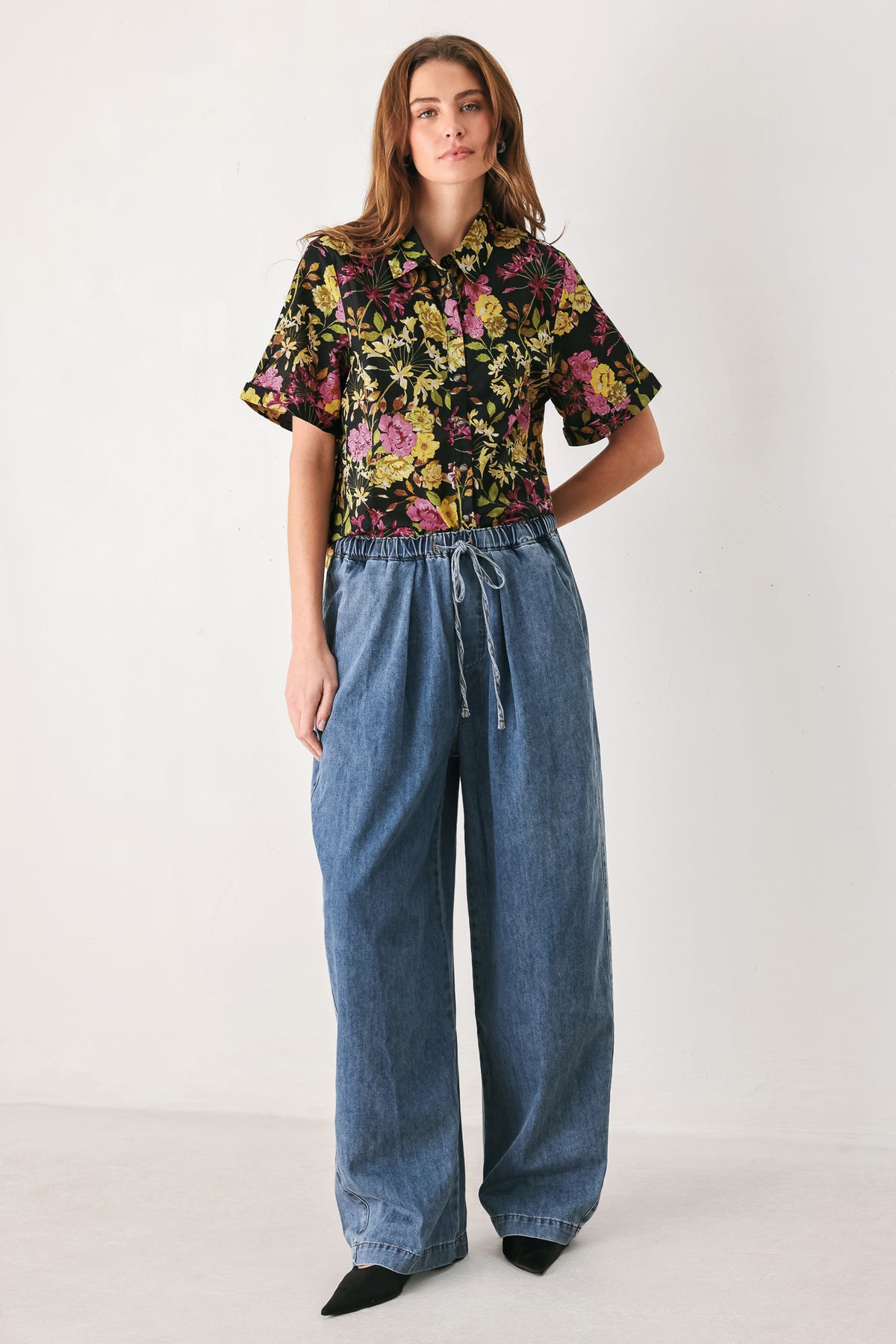 A woman wearing a black short-sleeve button-up shirt with a vibrant multicolor floral print in pink, yellow, and green | FREEMARKET