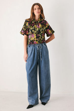 A woman wearing a black short-sleeve button-up shirt with a vibrant multicolor floral print in pink, yellow, and green | FREEMARKET