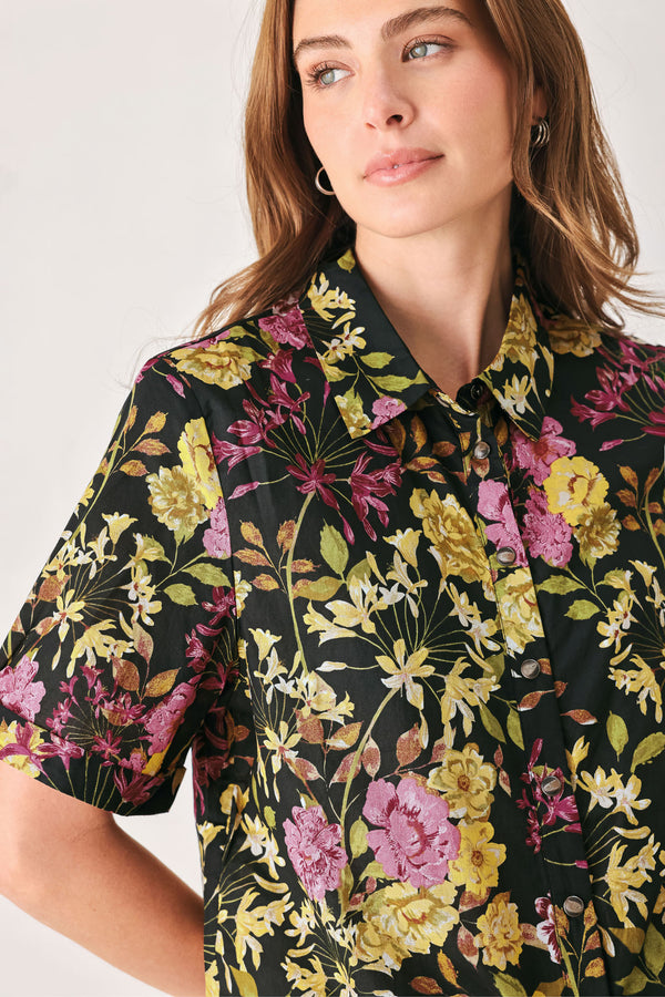 A woman wearing a black short-sleeve button-up shirt with a vibrant multicolor floral print in pink, yellow, and green | FREEMARKET