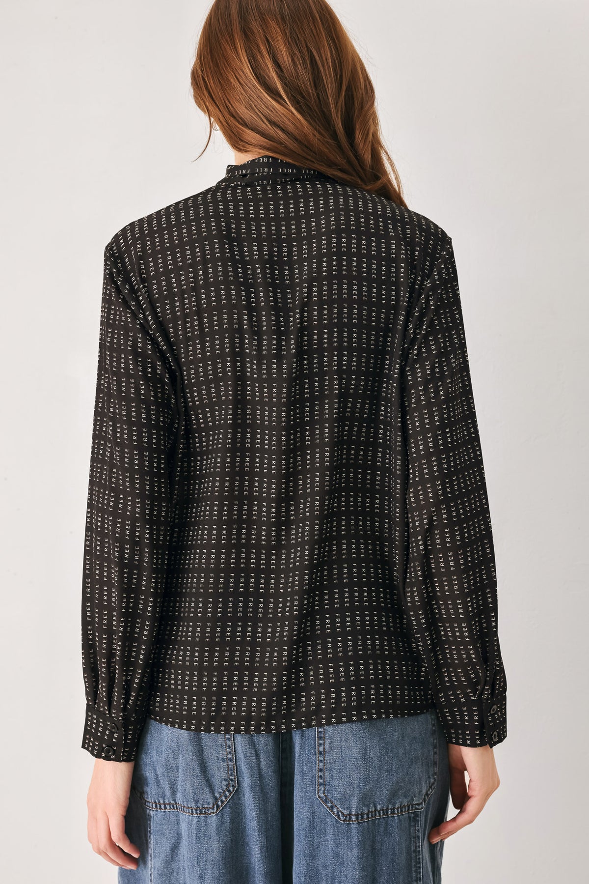 Person wearing a shirt with the word "FREE" printed on and wide-leg jeans on a plain background | FREEMARKET