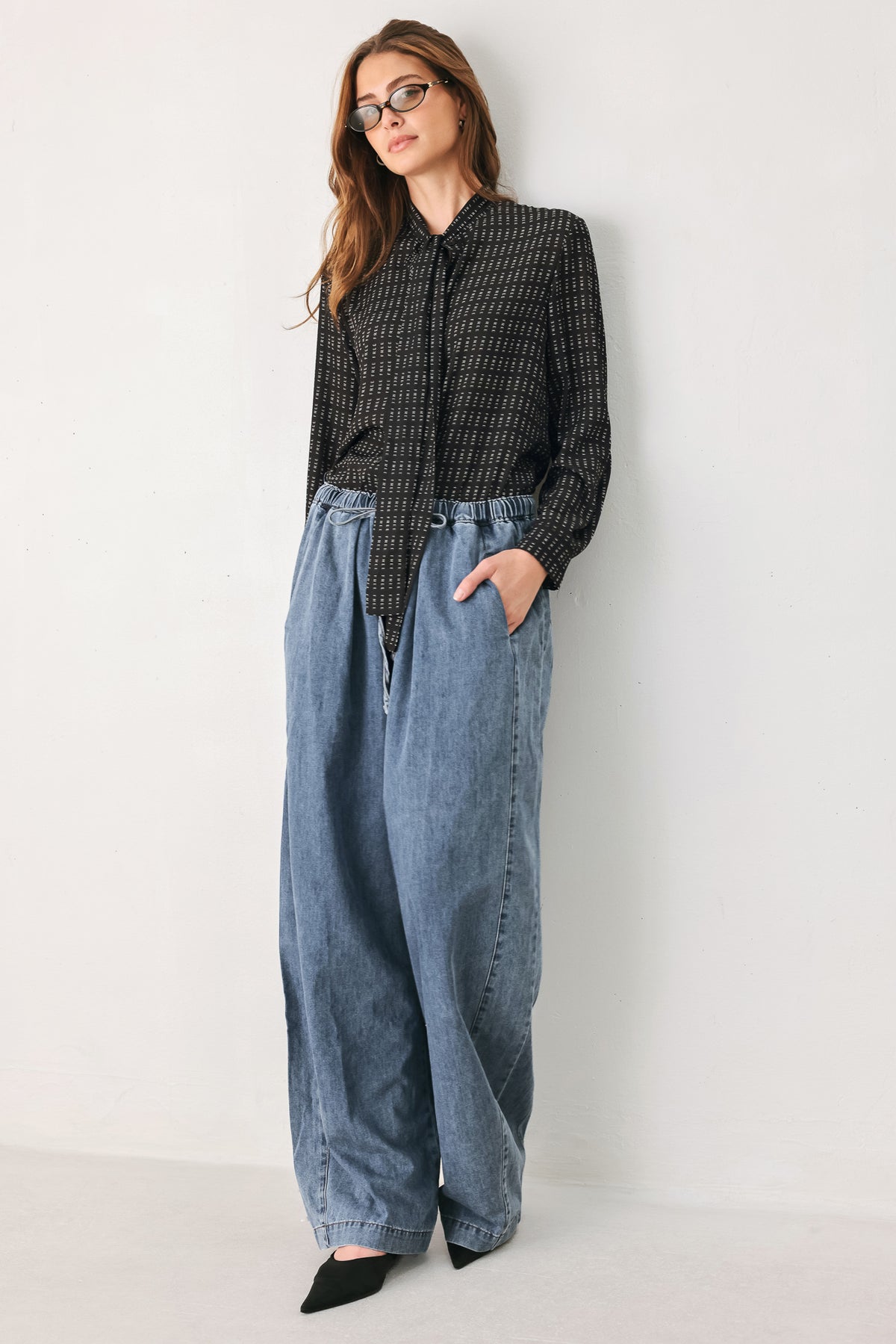 Person wearing a shirt with the word "FREE" printed on and wide-leg jeans on a plain background | FREEMARKET