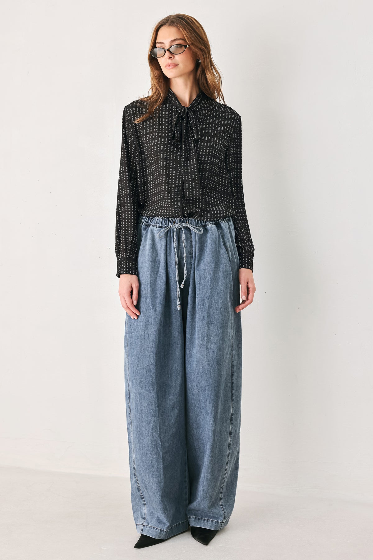 Person wearing a shirt with the word "FREE" printed on and wide-leg jeans on a plain background | FREEMARKET