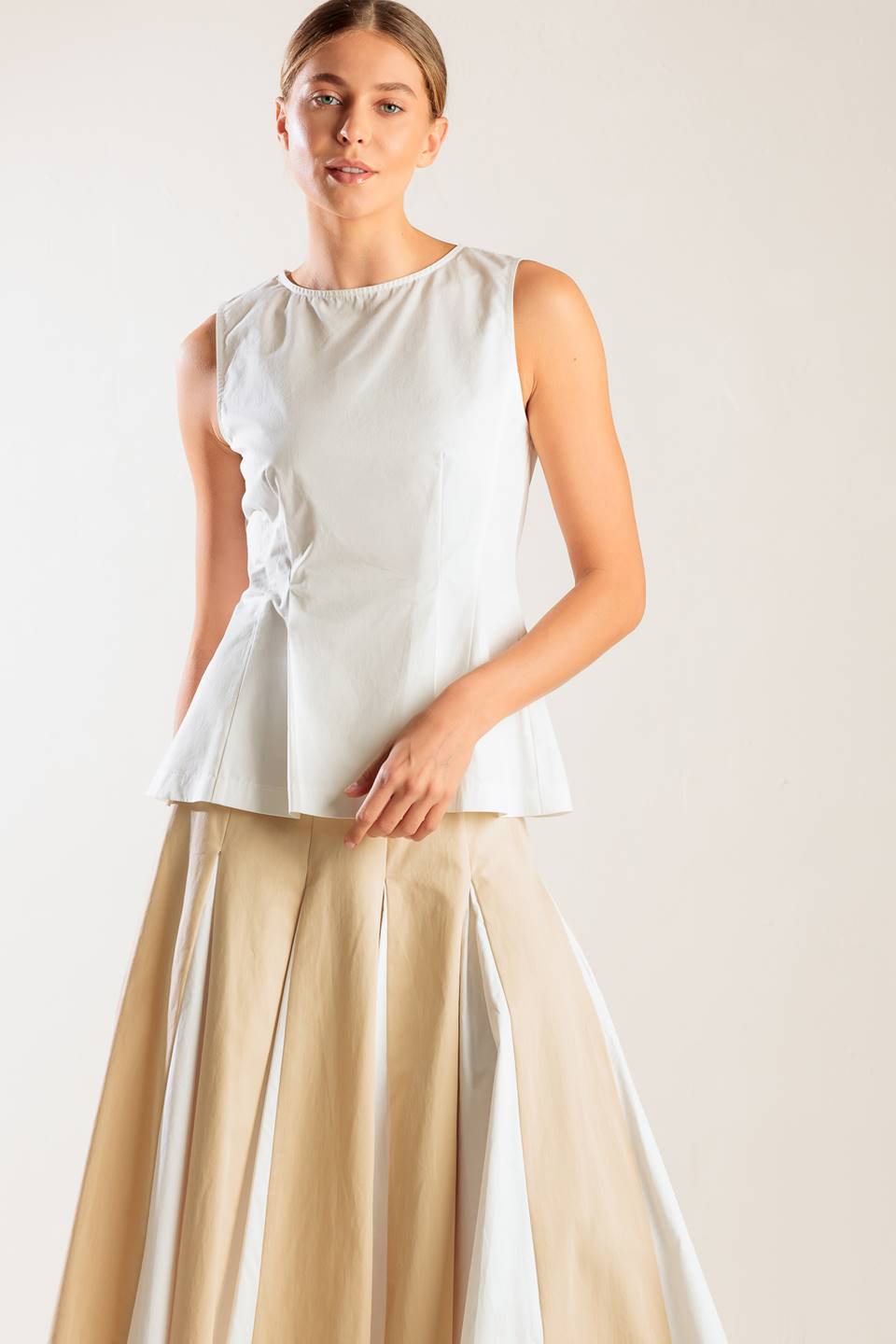 A solid, sleeveless, white woven top featuring round neckline and peplum