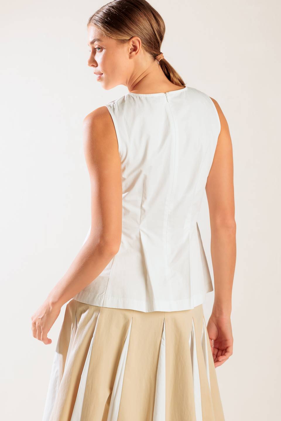 A solid, sleeveless, white woven top featuring round neckline and peplum