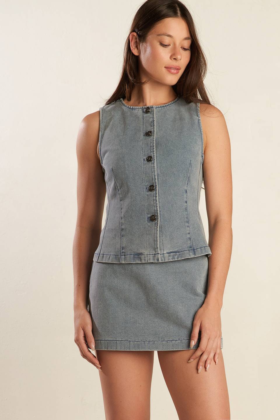 A sleeveless, washed denim vest featuring round neckline, and front button closure.