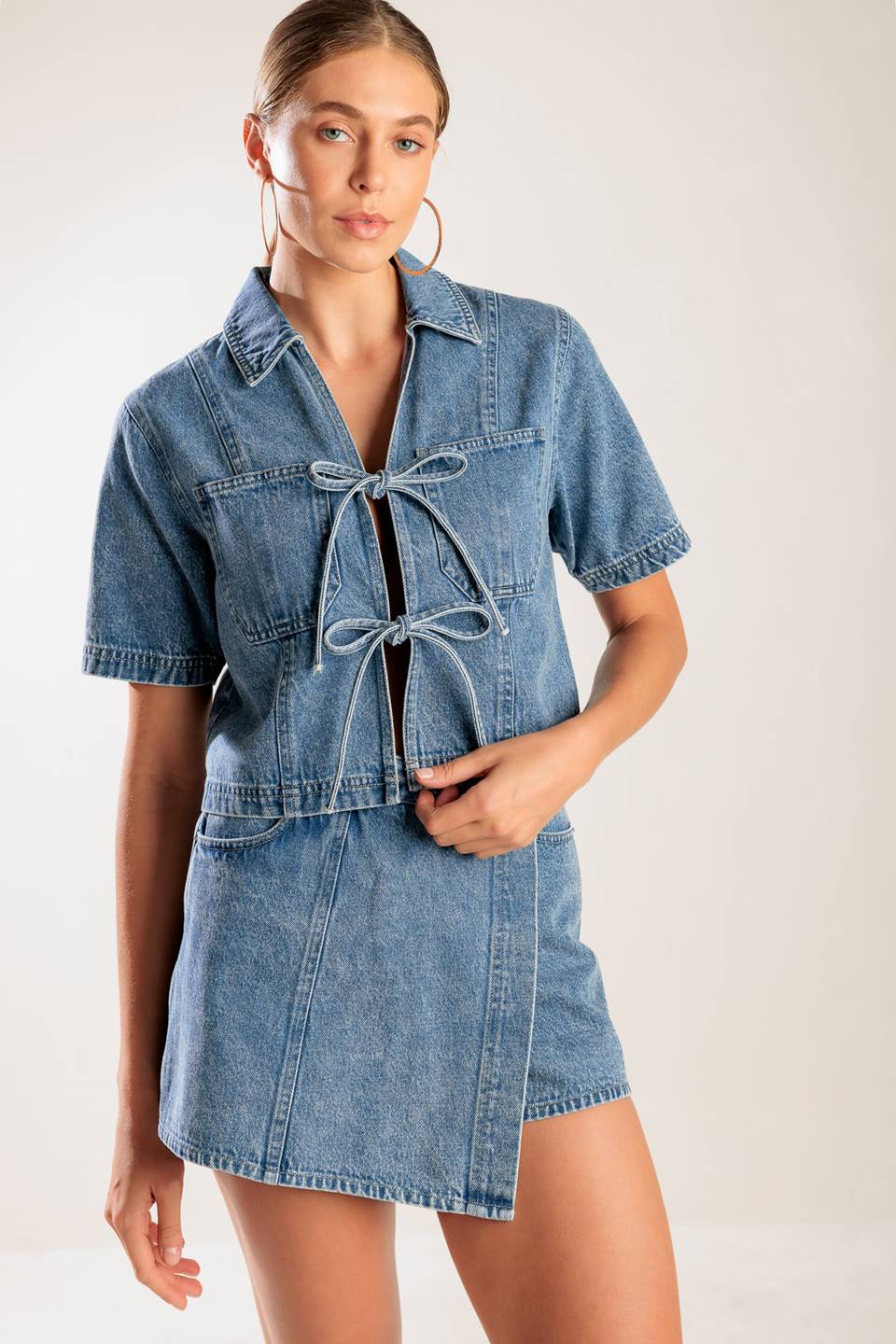 A washed denim top featuring collar, open front with bow ties, short sleeve and pockets.