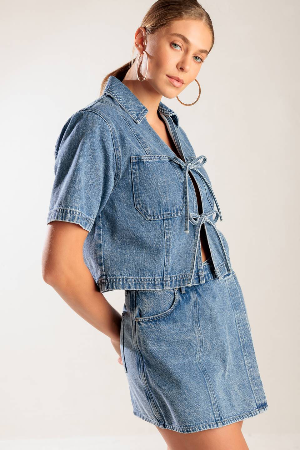 A washed denim top featuring collar, open front with bow ties, short sleeve and pockets.