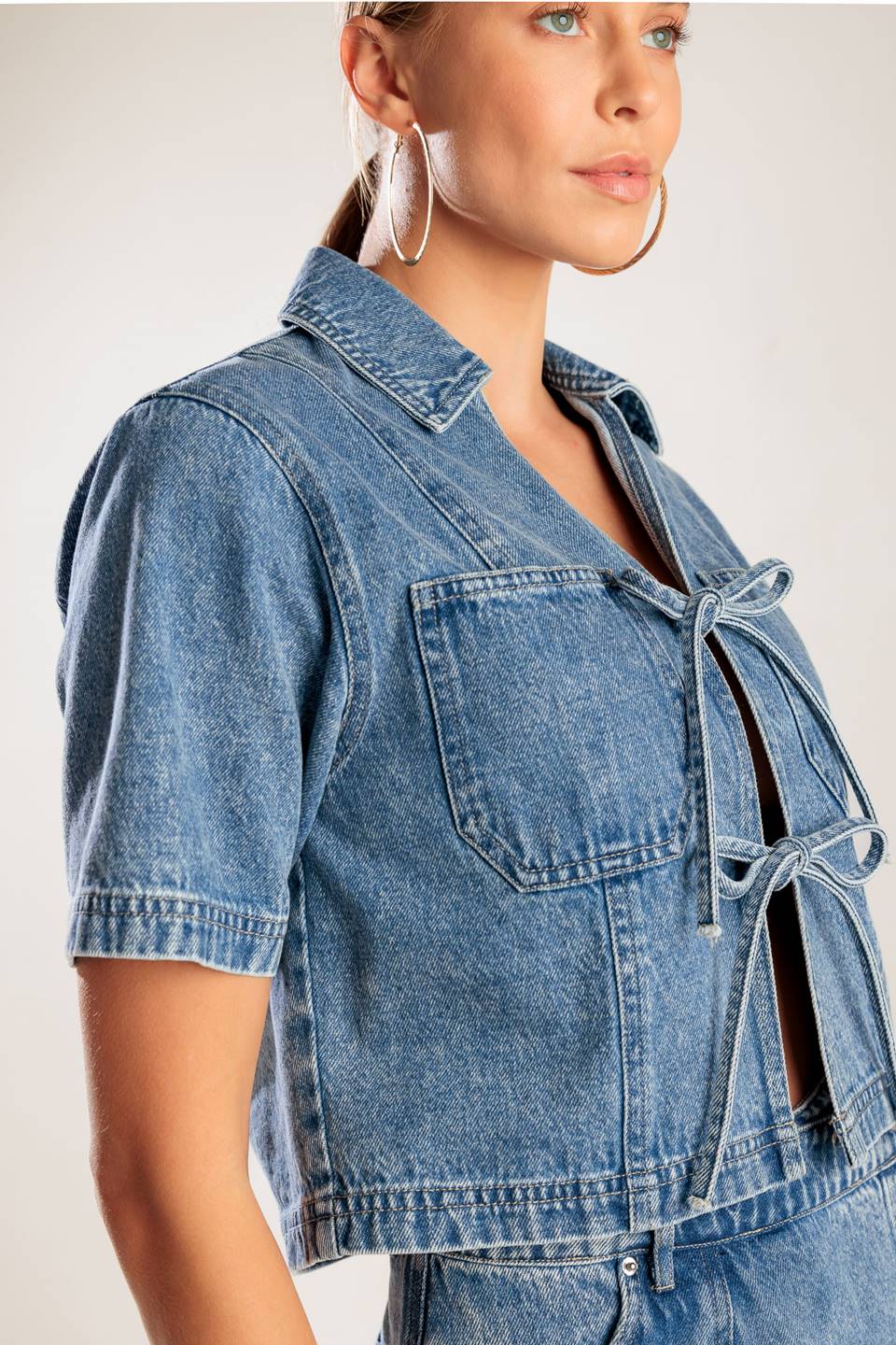 A washed denim top featuring collar, open front with bow ties, short sleeve and pockets.