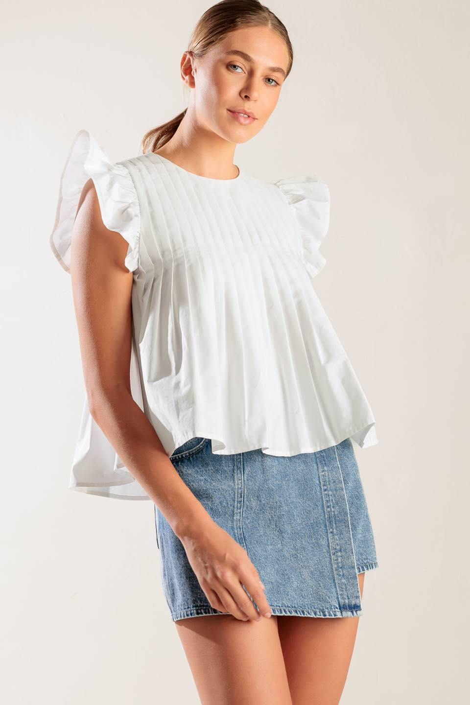 A solid white woven top featuring a round neckline, knife pleats, ruffled short sleeves and back neck button closure.