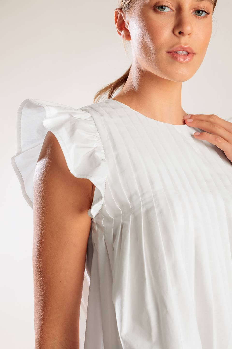 A solid white woven top featuring a round neckline, knife pleats, ruffled short sleeves and back neck button closure