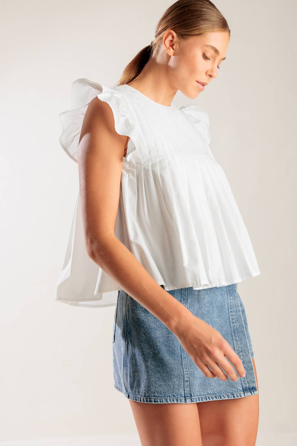 A solid white woven top featuring a round neckline, knife pleats, ruffled short sleeves and back neck button closure