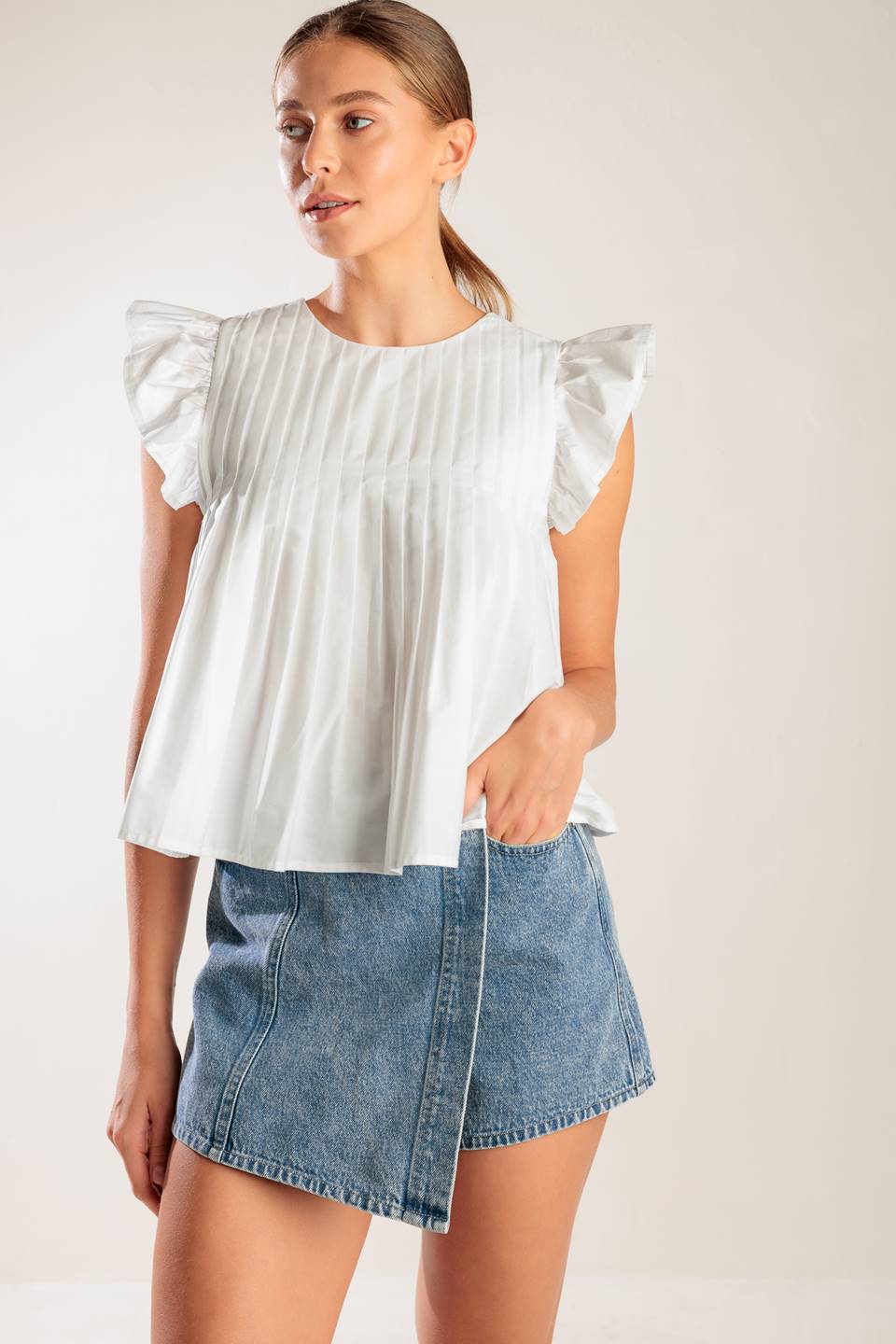 A solid white woven top featuring a round neckline, knife pleats, ruffled short sleeves and back neck button closure