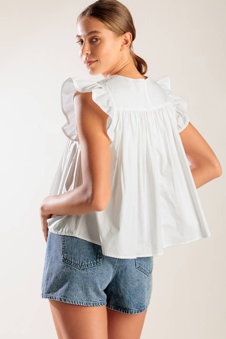 A solid white woven top featuring a round neckline, knife pleats, ruffled short sleeves and back neck button closure