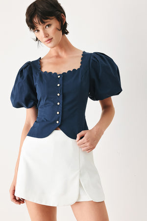 Woman wearing a blue blouse with puffed sleeves and a white skirt on a white background