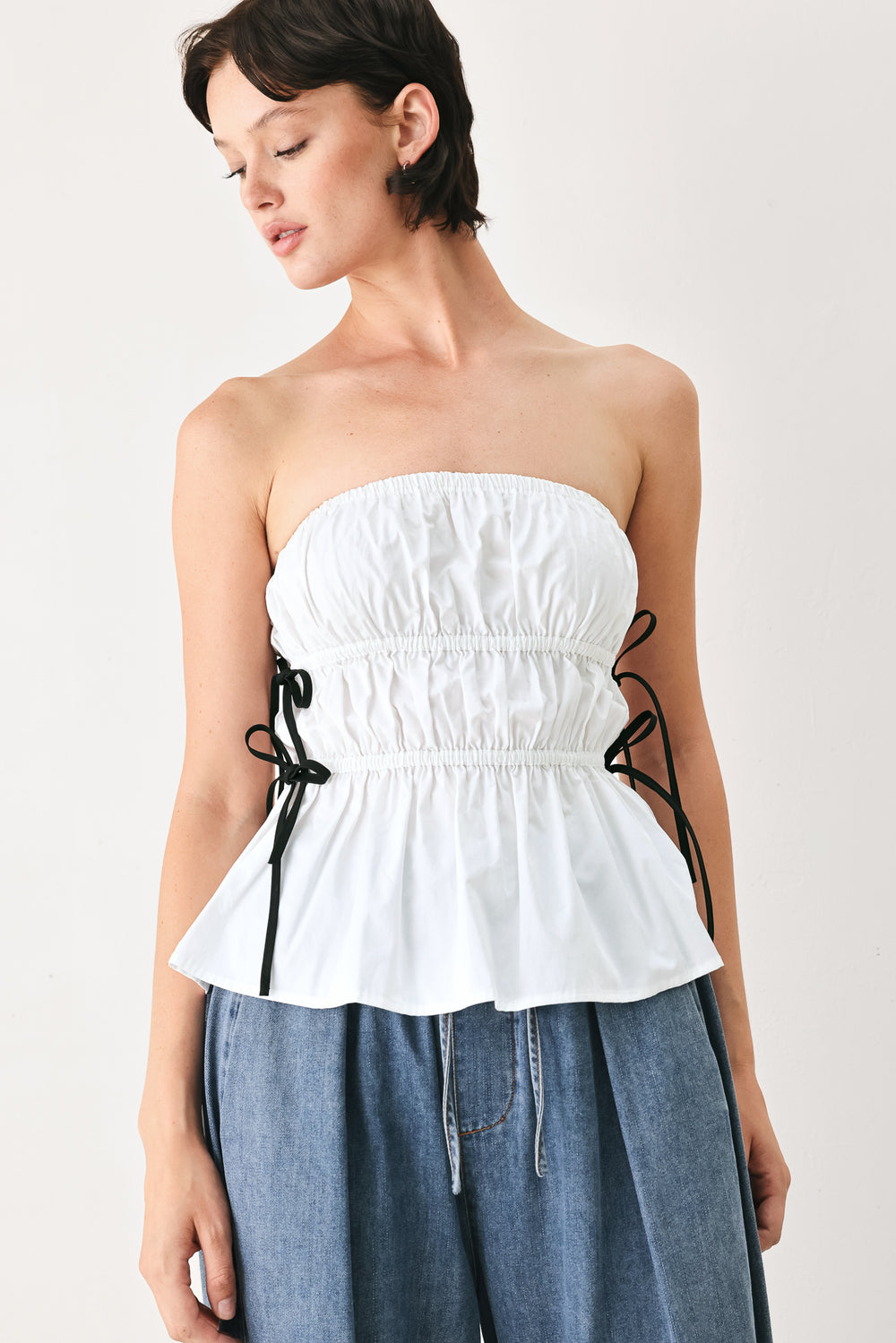 Woman wearing a white strapless top with black side ribbon bow ties | FREEMARKET
