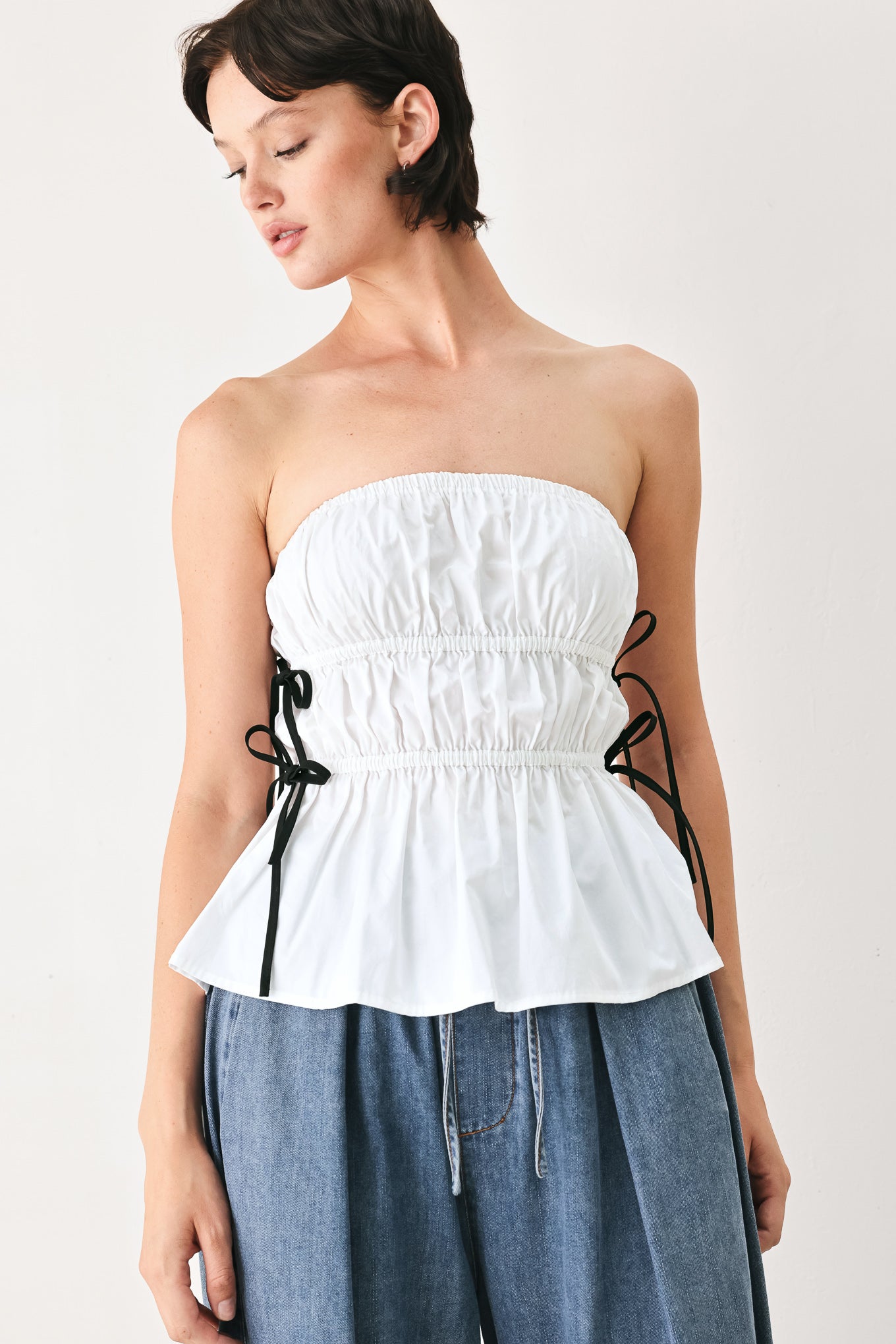 Woman wearing a white strapless top with black side ribbon bow ties | FREEMARKET
