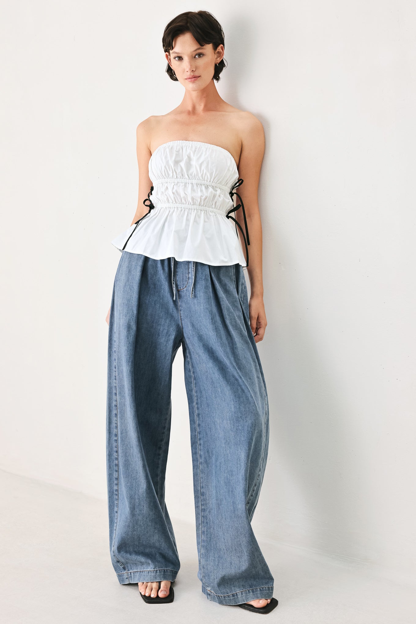Woman wearing a white strapless top with black side ribbon bow ties | FREEMARKET