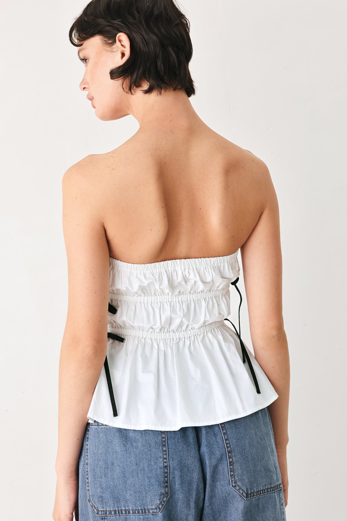 Woman wearing a white strapless top with black side ribbon bow ties | FREEMARKET