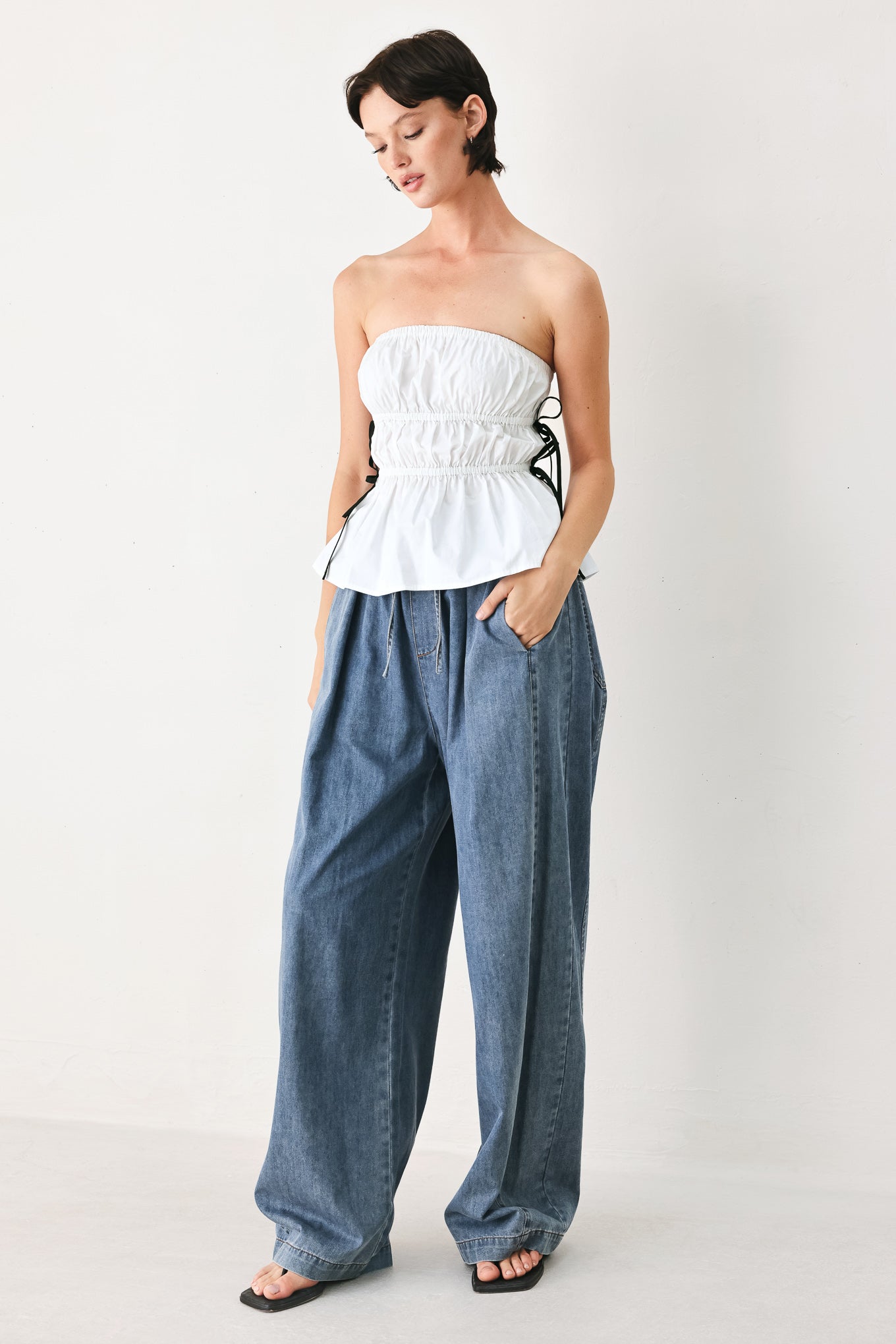 Woman wearing a white strapless top with black side ribbon bow ties | FREEMARKET