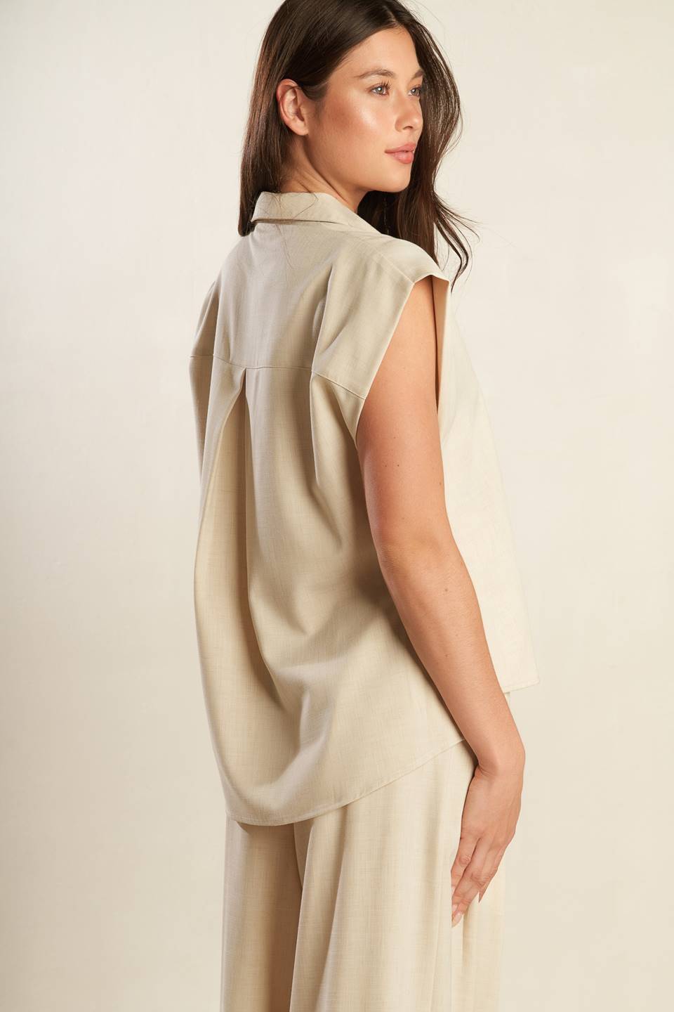 A beige, sleeveless, front button-down, solid woven shirt with collar neck.