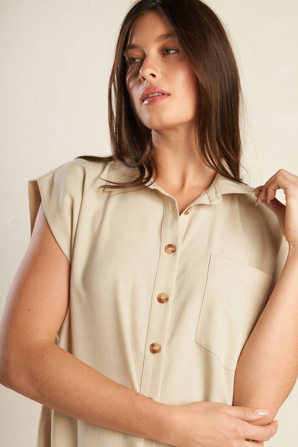 A beige, sleeveless, front button-down, solid woven shirt with collar neck.