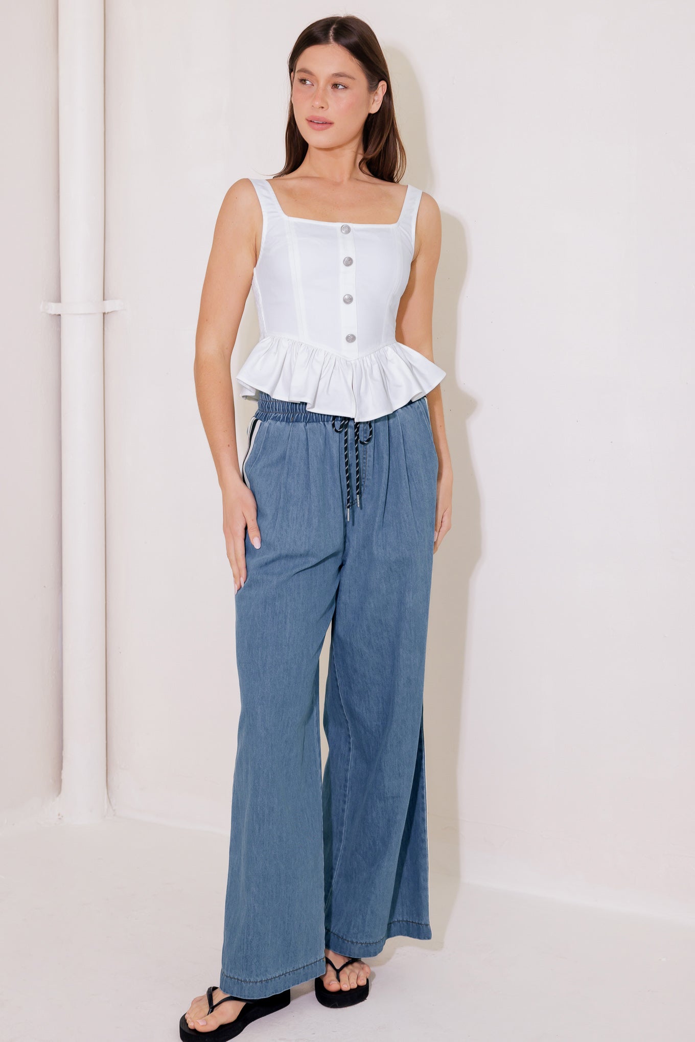 A solid woven top featuring square neckline, sleeveless, front button trim, ruffled peplum and smocked back bodice