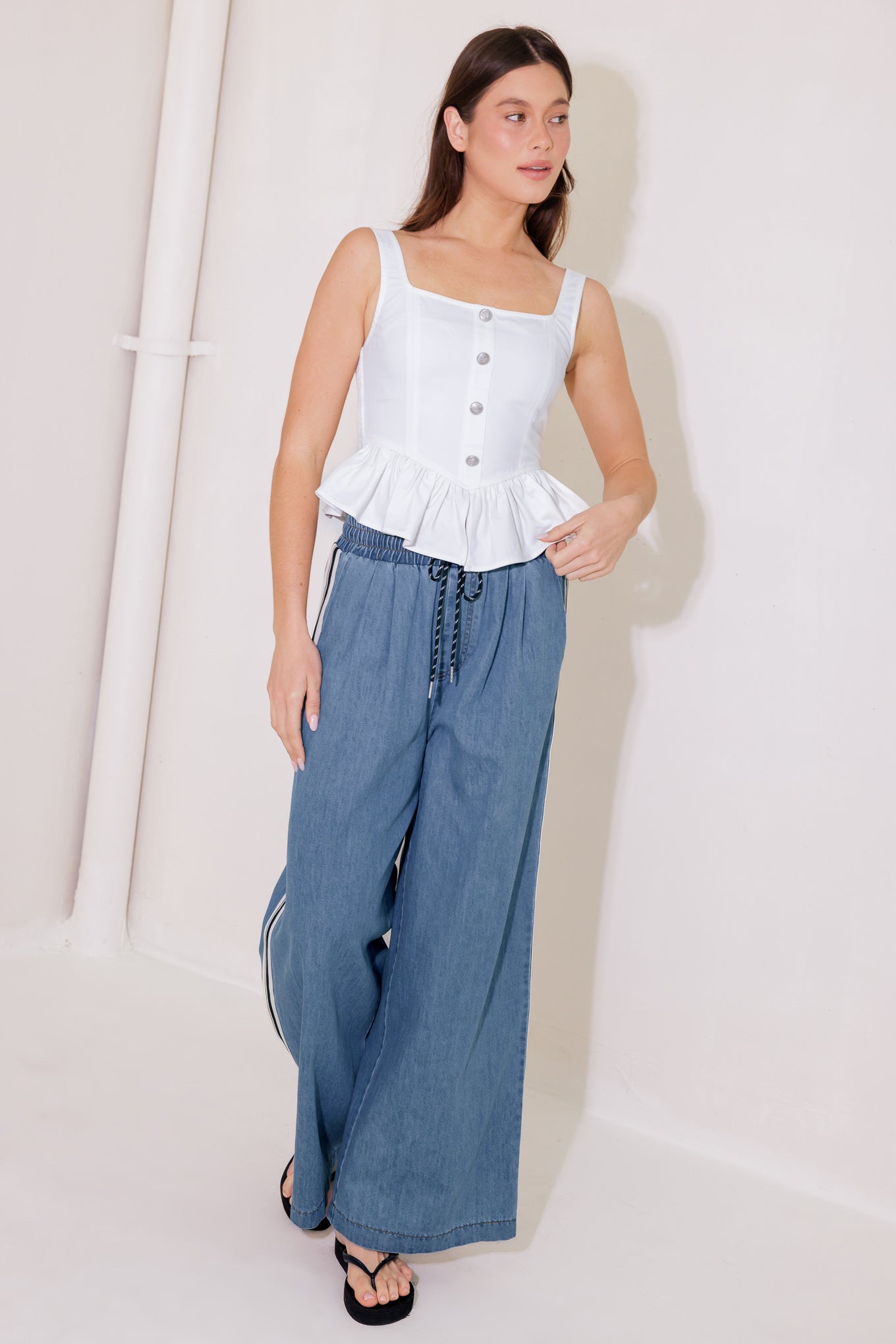 A solid woven top featuring square neckline, sleeveless, front button trim, ruffled peplum and smocked back bodice