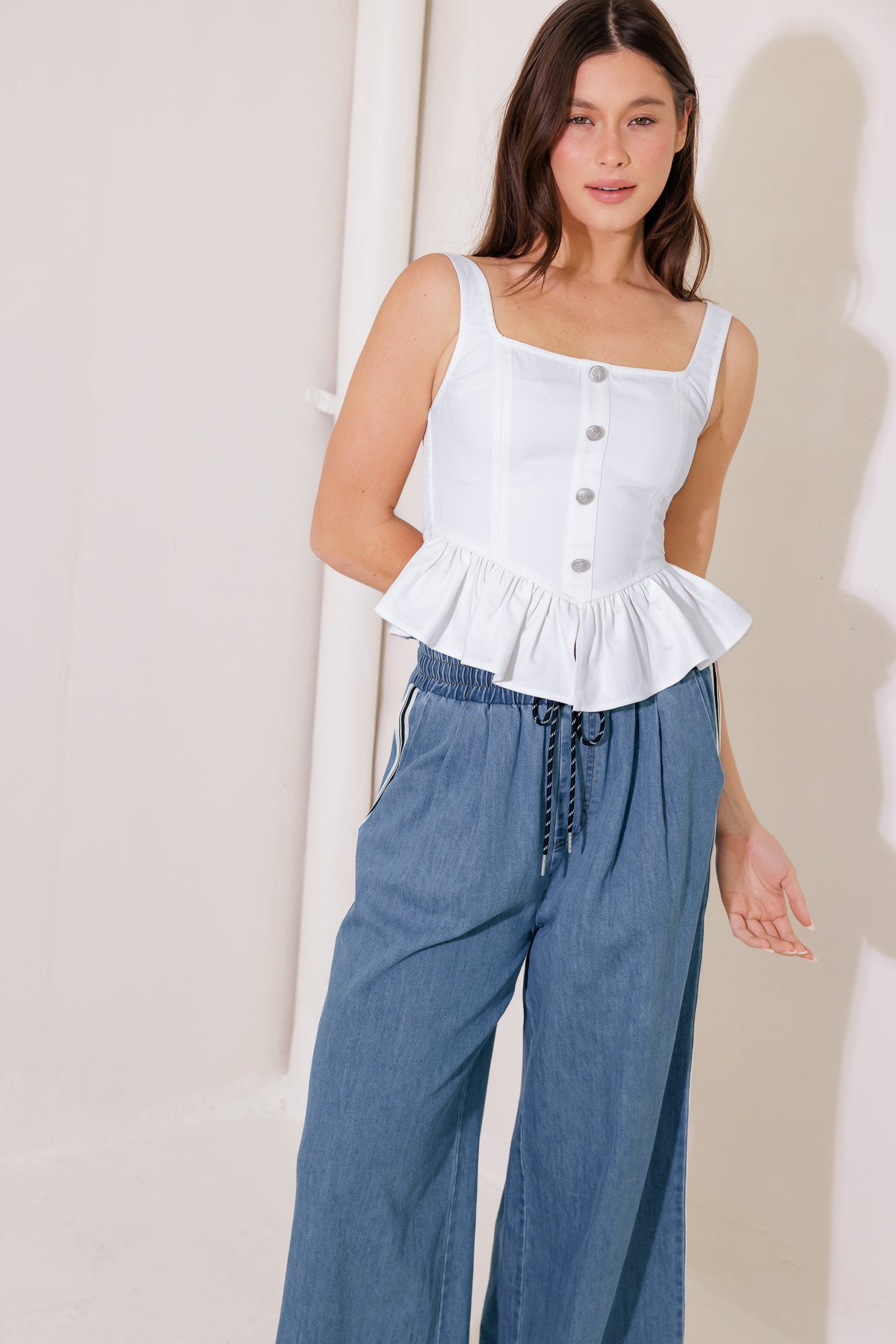 A solid woven top featuring square neckline, sleeveless, front button trim, ruffled peplum and smocked back bodice