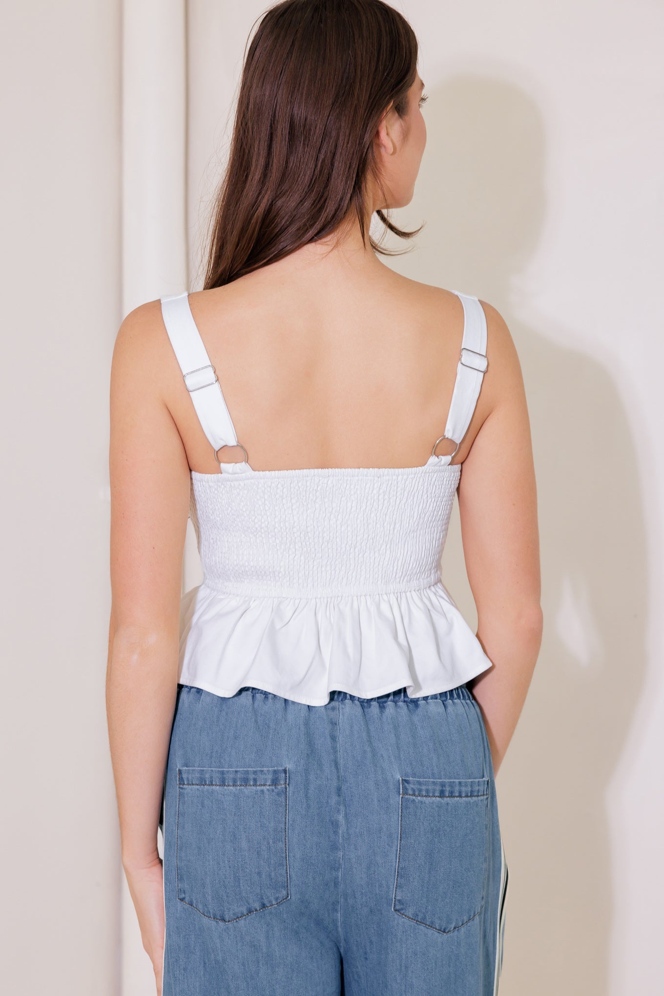 A solid woven top featuring square neckline, sleeveless, front button trim, ruffled peplum and smocked back bodice
