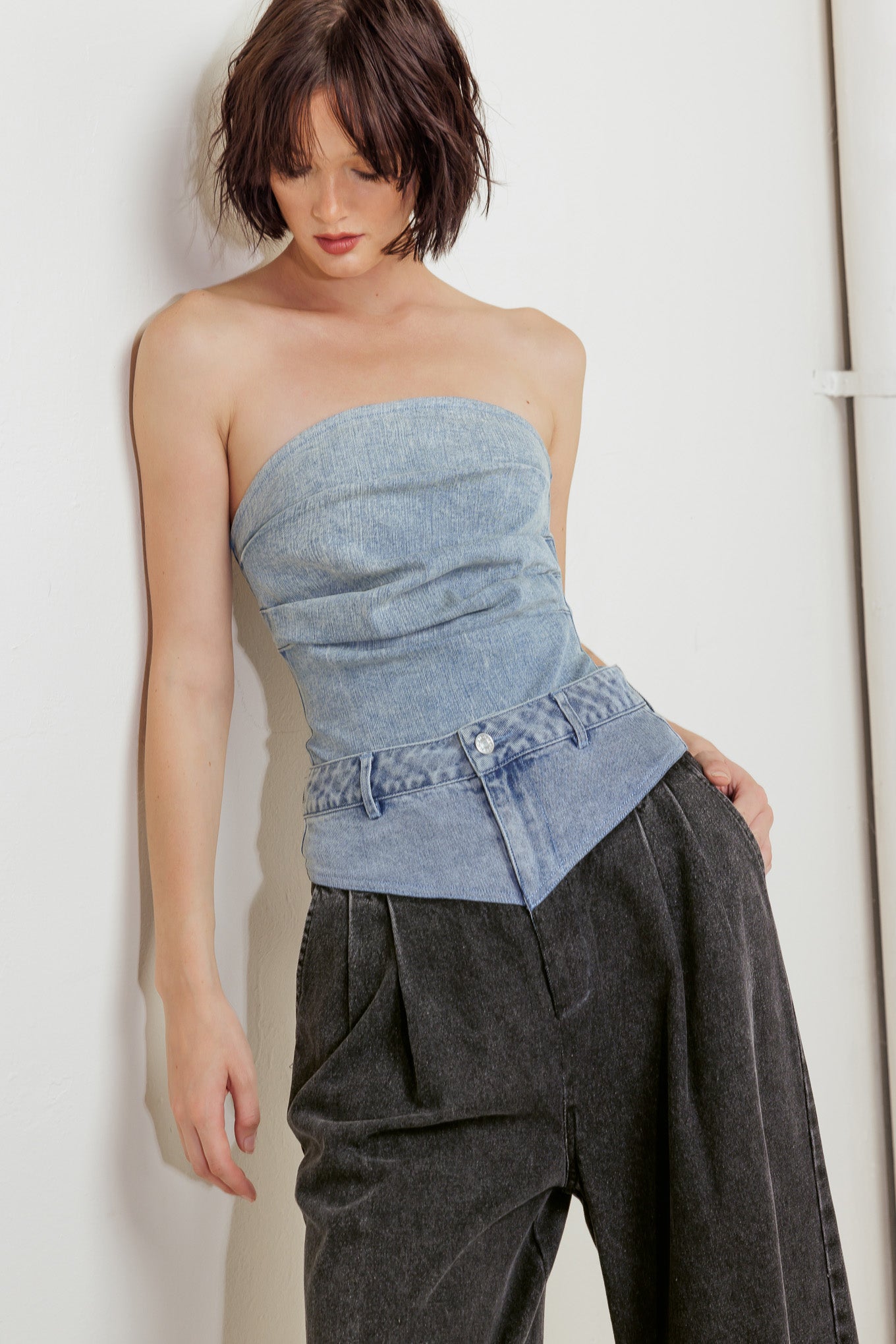 An acid-washed denim bodysuit featuring strapless, side shirring and bottom snap button closure