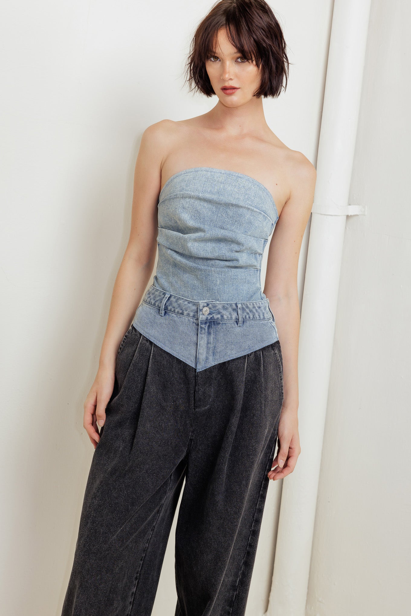 An acid-washed denim bodysuit featuring strapless, side shirring and bottom snap button closure