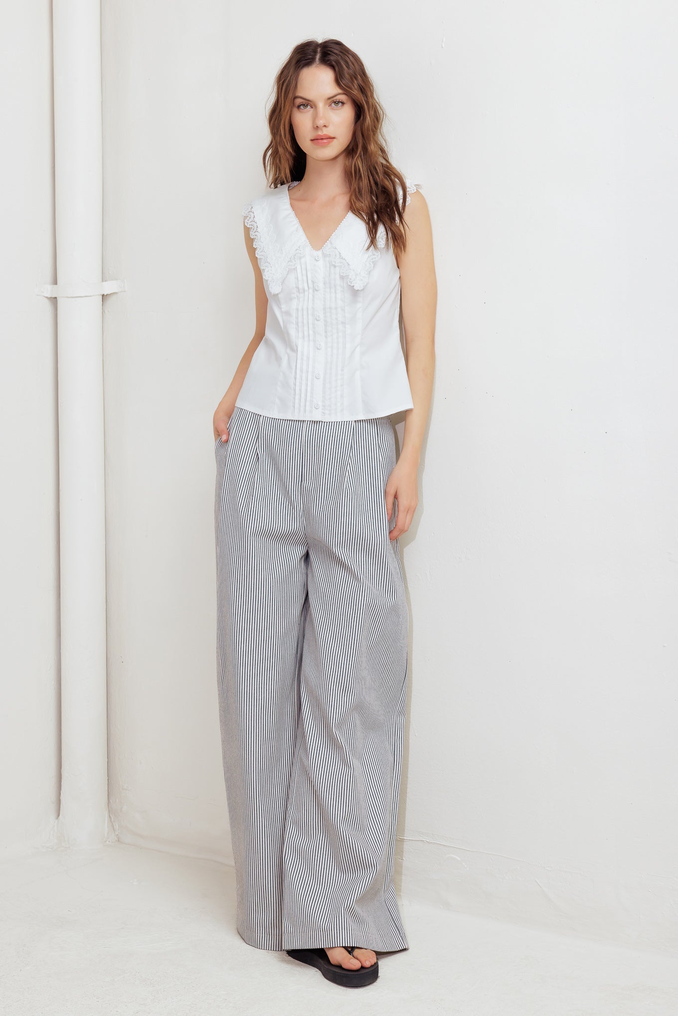 A solid woven top featuring V neckline, peter pan collar with lace trim, sleeveless, pin tuck front and button down closure